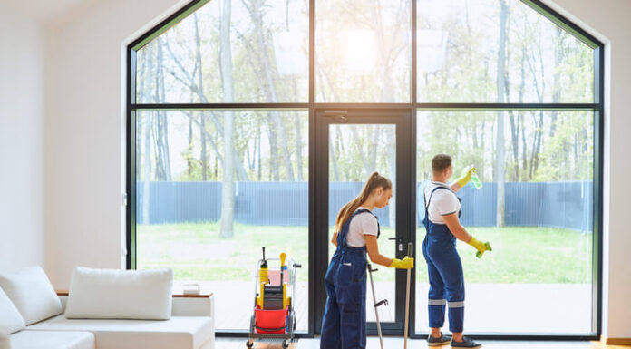 Young cleaners in blue uniform mopping wooden floor and cleaning big panoramic window