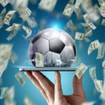 Dollars are falling on the background of a hand with a smartphone and a soccer ball