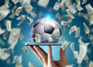 Dollars are falling on the background of a hand with a smartphone and a soccer ball