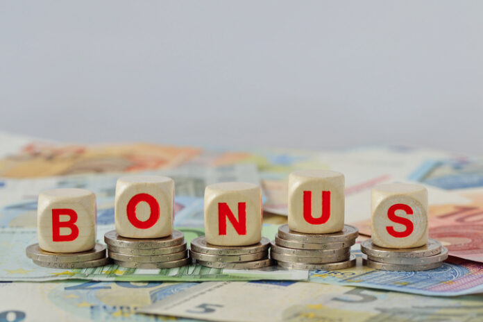 Wooden blocks with the word Bonus on coins and banknotes - Concept of economic bonus and financial aid Wooden blocks with the word Bonus on coins and banknotes