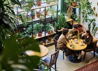 Two intercultural friends or dates having chat in cafe while sitting by table next to young woman drinking latte and listening to their discussion