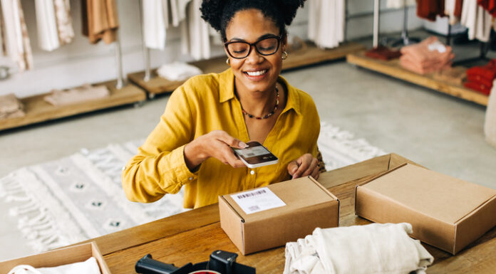 Is Dropshipping Worth It In 2024? Female dropshipper uses a smartphone to scan the QR code for an online clothing order