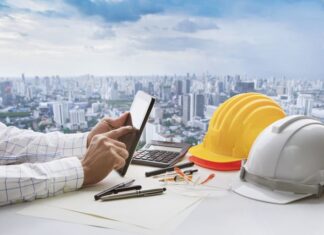 Hand of business man touching on computer tablet screen and safety helmet on working table against cities of high building for accommodation
