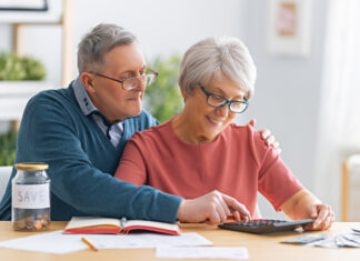Elderly married couple sitting at the desk with a paper receipt in hands are calculating expenses, managing the budget.