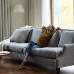 Happy carefree young female homeowner resting on comfortable couch.