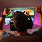 4RaBet Business Model Back view of professional gamer wearing headphones celebrating victory while playing online video game at home