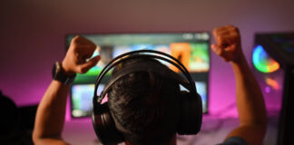 4RaBet Business Model Back view of professional gamer wearing headphones celebrating victory while playing online video game at home
