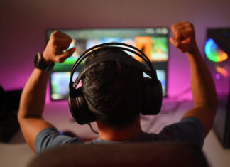 Back view of professional gamer wearing headphones celebrating victory while playing online video game at home