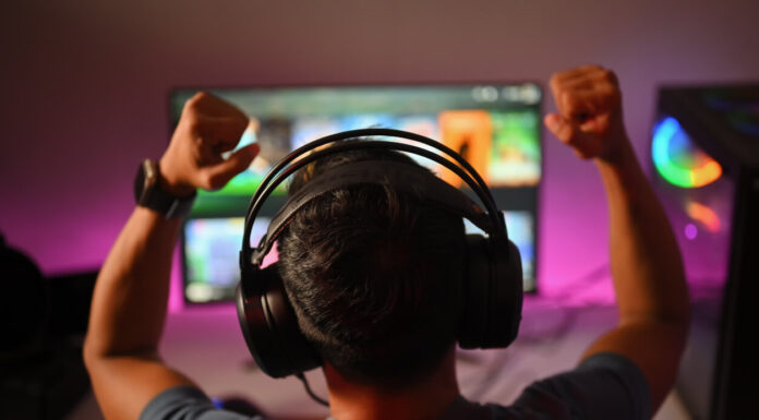 Back view of professional gamer wearing headphones celebrating victory while playing online video game at home