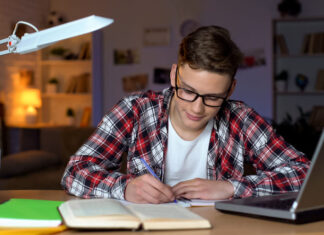 Tips for Creating a Successful Homework Routine Student in glasses doing homework, writing essay, open book and laptop on table