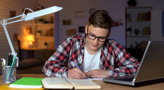 Tips for Creating a Successful Homework Routine Student in glasses doing homework, writing essay, open book and laptop on table