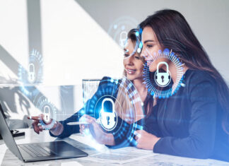 Businesswomen working together finger pointing at laptop on desk, smiling portraits. Glowing padlock icon with circuit hud. Cybersecurity and data protection.
