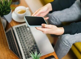 McKinney Consulting’s Steve McKinney Highlights the Disadvantages and Hidden Costs of Not Hiring Executive Search Firms Person Using Smartphone and Laptop in Office Setting