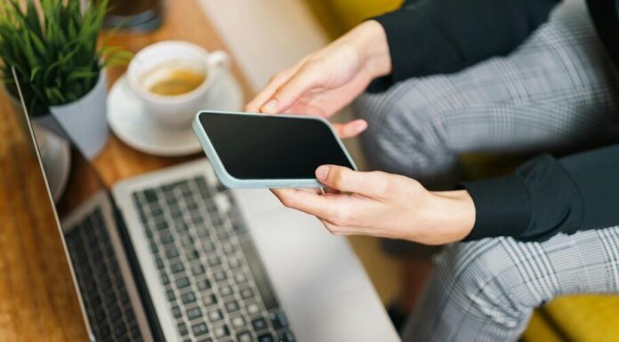 Person Using Smartphone and Laptop in Office Setting