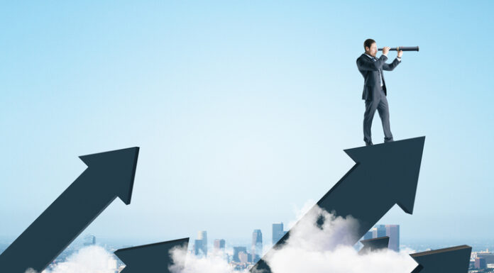 Businessman standing on abstract arrow and using telescope to look into the distance on city background.