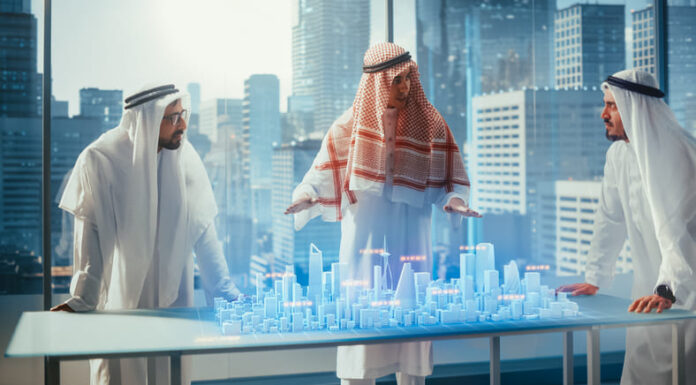 Business Developers in Traditional Clothes Discuss Investing Opportunities Based on Holographic Augmented Reality 3D City Model in Their Modern Office in a Skyscraper.