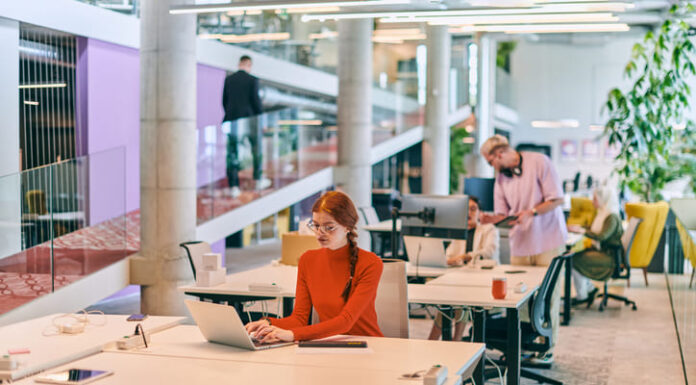 The Profound Benefits of Coworking Spaces in Amsterdam professional businesswoman with orange hair sitting at her laptop, epitomizing innovation and productivity in her contemporary workspace