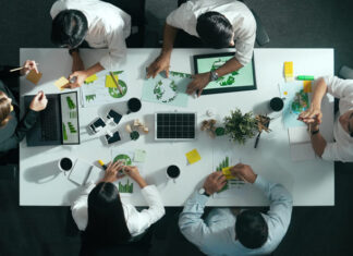 Environmental Heroes and Villains – What Separates Truly Sustainable Organisations from those that Play Around the Edges?  Top down view of business team discussing about using clean energy and sustainable investment at meeting table