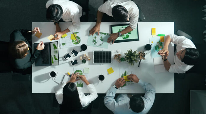 Environmental Heroes and Villains – What Separates Truly Sustainable Organisations from those that Play Around the Edges? Top down view of business team discussing about using clean energy and sustainable investment at meeting table