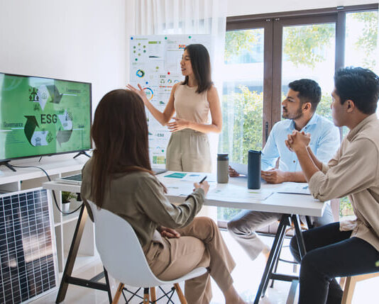 Asian woman lead young group of multiethnic businesspeople in team meeting, using laptop computer for ESG topic presentation on monitor.