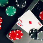Red And Black Casino Chips On A Table With A Laptop And Playing Cards