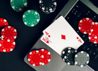 Red And Black Casino Chips On A Table With A Laptop And Playing Cards