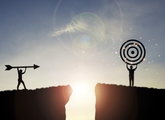 The Dangers of Being Outcome-Obsessed Silhouette men throwing arrow and holding dartboard on mountain with blue sky and sunlight for achievement objectives target and vision