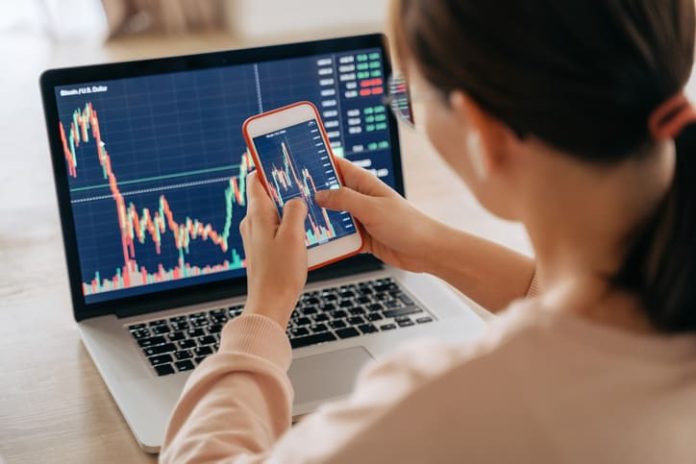 Woman crypto trader investor broker using smartphone app and laptop executing financial stock trade market trading order to buy or sell cryptocurrency - API