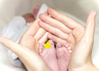 Person holding babys toe with yellow petaled flower