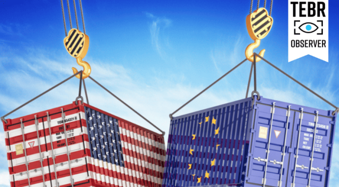 After Tariffs on Canada, Mexico, and China, Trump Looks Toward the EU cargo containers with USA and European Union flags hoisted by crane hooks on blue cloudy sky