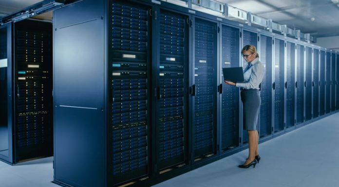 Client Server Networks: What are they, and what are the Advantages? Female IT Technician Stands Near Rack Cabinet and Runs Maintenance Program on Laptop, Controls Operational Server's Optimal Functioning.