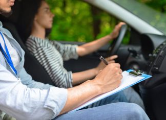 Cropped of male instructor examinating female student, taking notes at test chart while sitting by young woman driving automobile, side view, copy space, closeup.