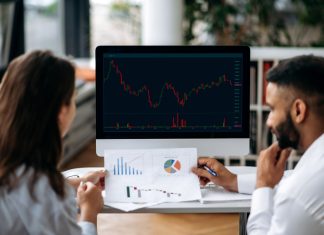 Smart successful business colleagues in trading, sitting in modern office, looking at screen with stock market graphs, analyzing dynamics, developing a strategy,
