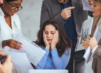 3 Reasons Saying ‘Yes’ is Stalling Your Professional Growth Frustrated millennial female worker sitting at table with colleagues, felling tired of working, out of focus, quarreling at business meeting