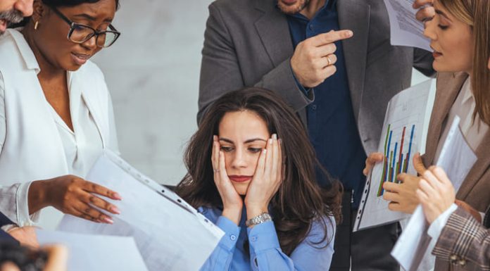 3 Reasons Saying ‘Yes’ is Stalling Your Professional Growth Frustrated millennial female worker sitting at table with colleagues, felling tired of working, out of focus, quarreling at business meeting