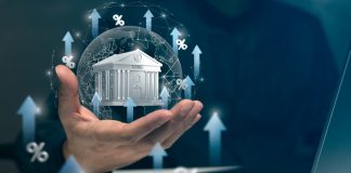 Real-Life Banking Scenarios for Tomorrow’s Financial Leaders A hand holds a virtual bank surrounded by arrows and percentage signs, symbolizing rising interest rates and banking growth trends.