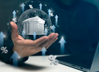 A hand holds a virtual bank surrounded by arrows and percentage signs, symbolizing rising interest rates and banking growth trends.
