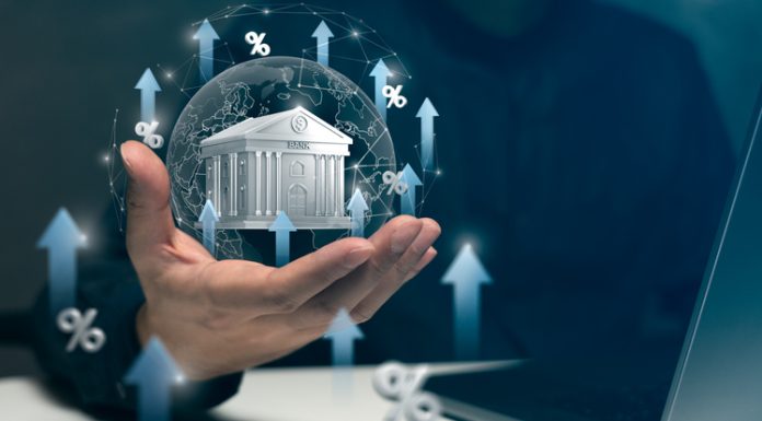 Real-Life Banking Scenarios for Tomorrow’s Financial Leaders A hand holds a virtual bank surrounded by arrows and percentage signs, symbolizing rising interest rates and banking growth trends.