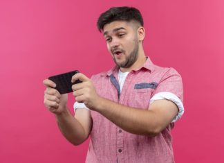 Young man wearing pink polo playing game on mobile phone