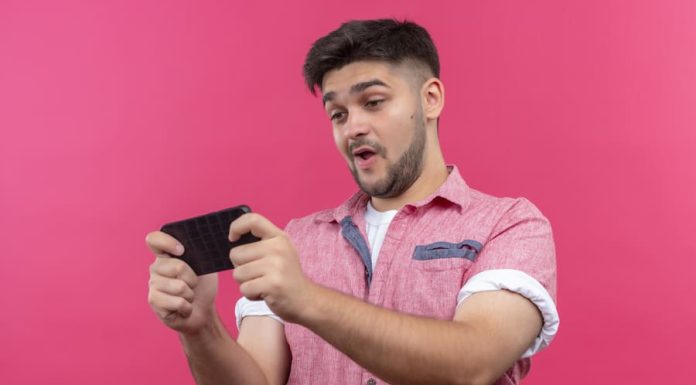 Young man wearing pink polo playing game on mobile phone