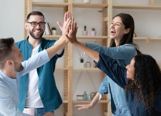 The Happiness Payoff: How Employee Wellbeing Drives Business Success l employees give high five celebrate shared team business success in office.