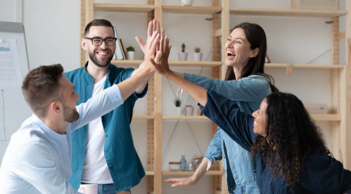 The Happiness Payoff: How Employee Wellbeing Drives Business Success l employees give high five celebrate shared team business success in office.