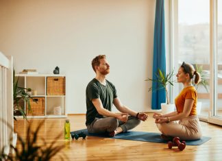 Young couple in lotus pose practicing Yoga together at home.