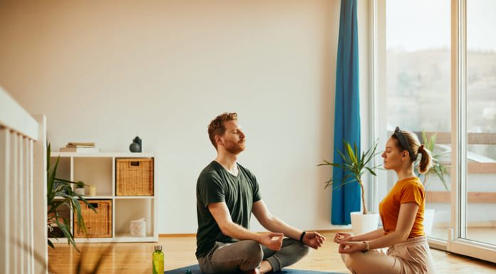 Young couple in lotus pose practicing Yoga together at home.