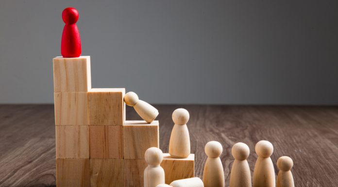 Leadership Dystopia – The Dangers of Leadership as a Reward Wooden people figures on top of wooden block in the concept of leadership