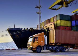 Truck transportation carrying forty-foot container leaving port terminal with ship and quay crane on the background
