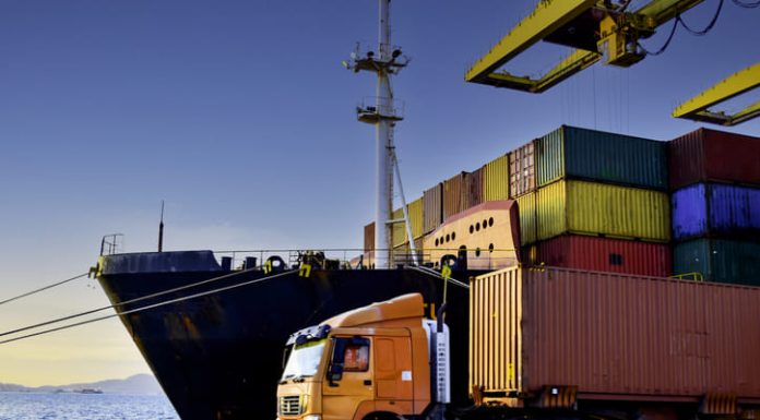 Truck transportation carrying forty-foot container leaving port terminal with ship and quay crane on the background