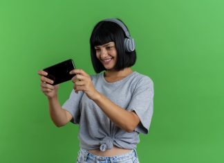 Smiling young brunette caucasian woman on headphones holds and looks at phone