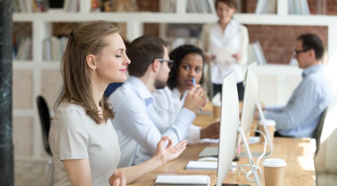 Peaceful millennial woman practice yoga in front of computer at workplace, calm female employee meditating controlling emotions and managing stress, worker sit in lotus position in office
