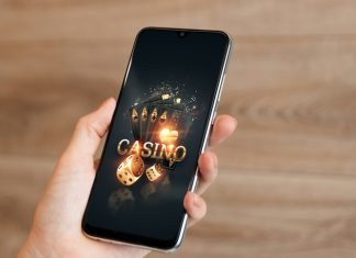In the hands of a smartphone with playing cards the inscription casino, black-gold background.
